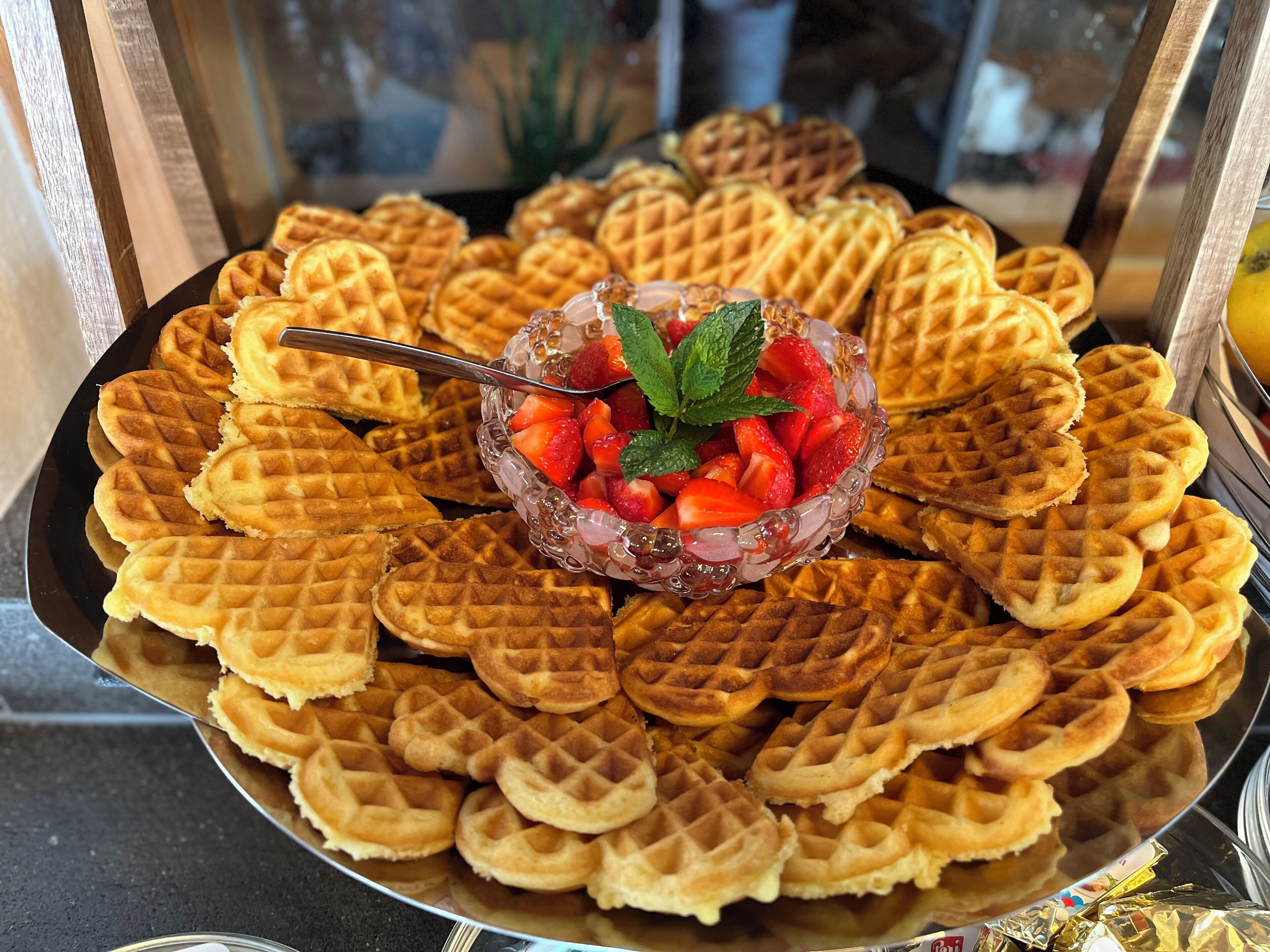 Una bandeja de waffles con forma de corazón, con un tazón de fresas y menta en el centro.