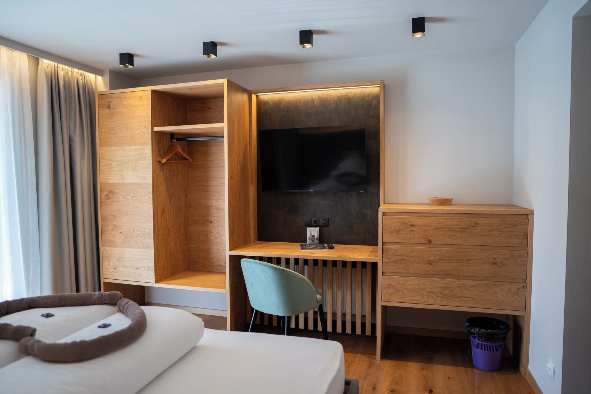 Una habitación de hotel moderna con un escritorio de madera, una silla, un televisor, una cama y un vestidor.
