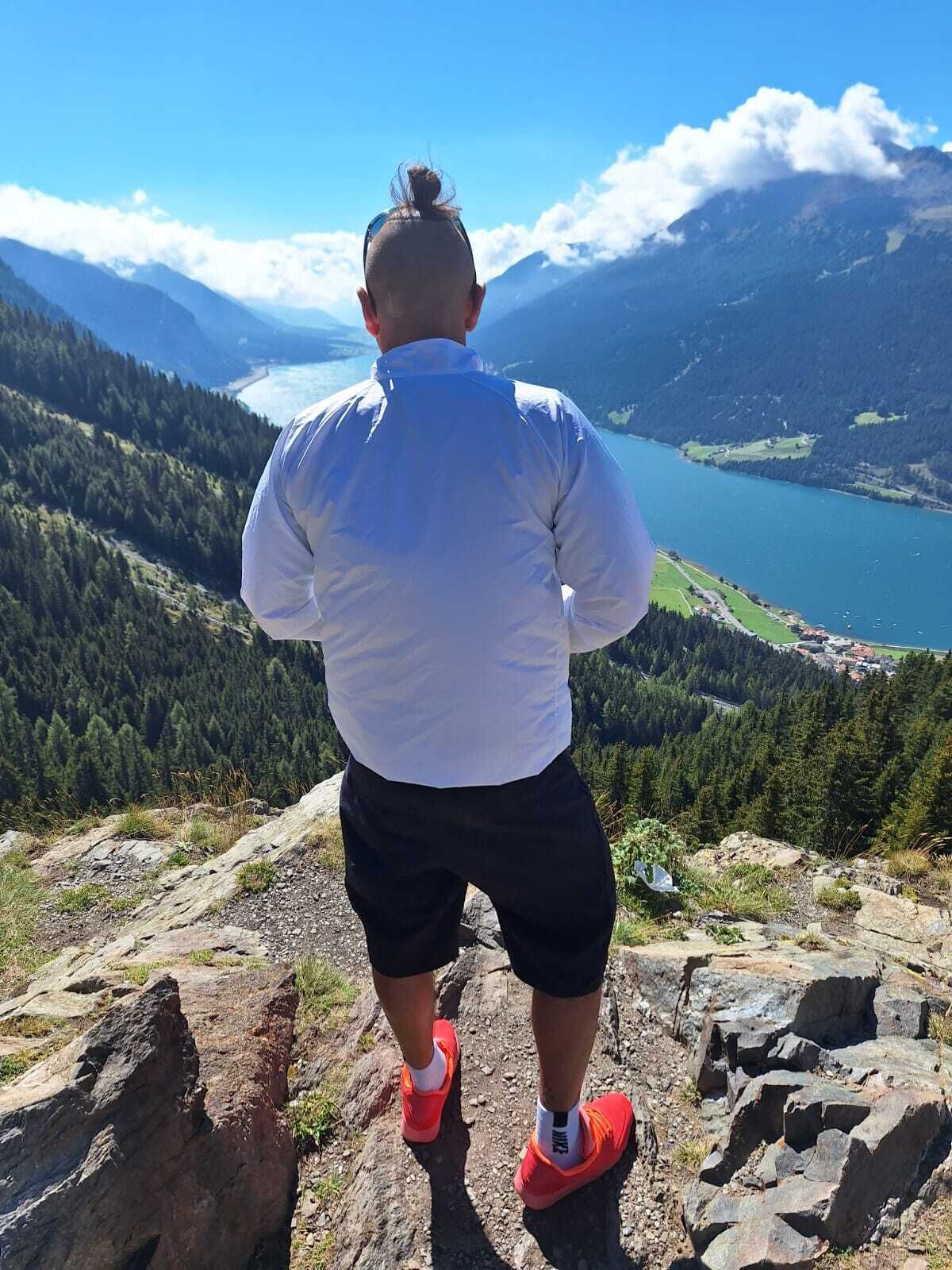 Iemand staat op een rotsachtige richel met uitzicht op een meer en bergen.