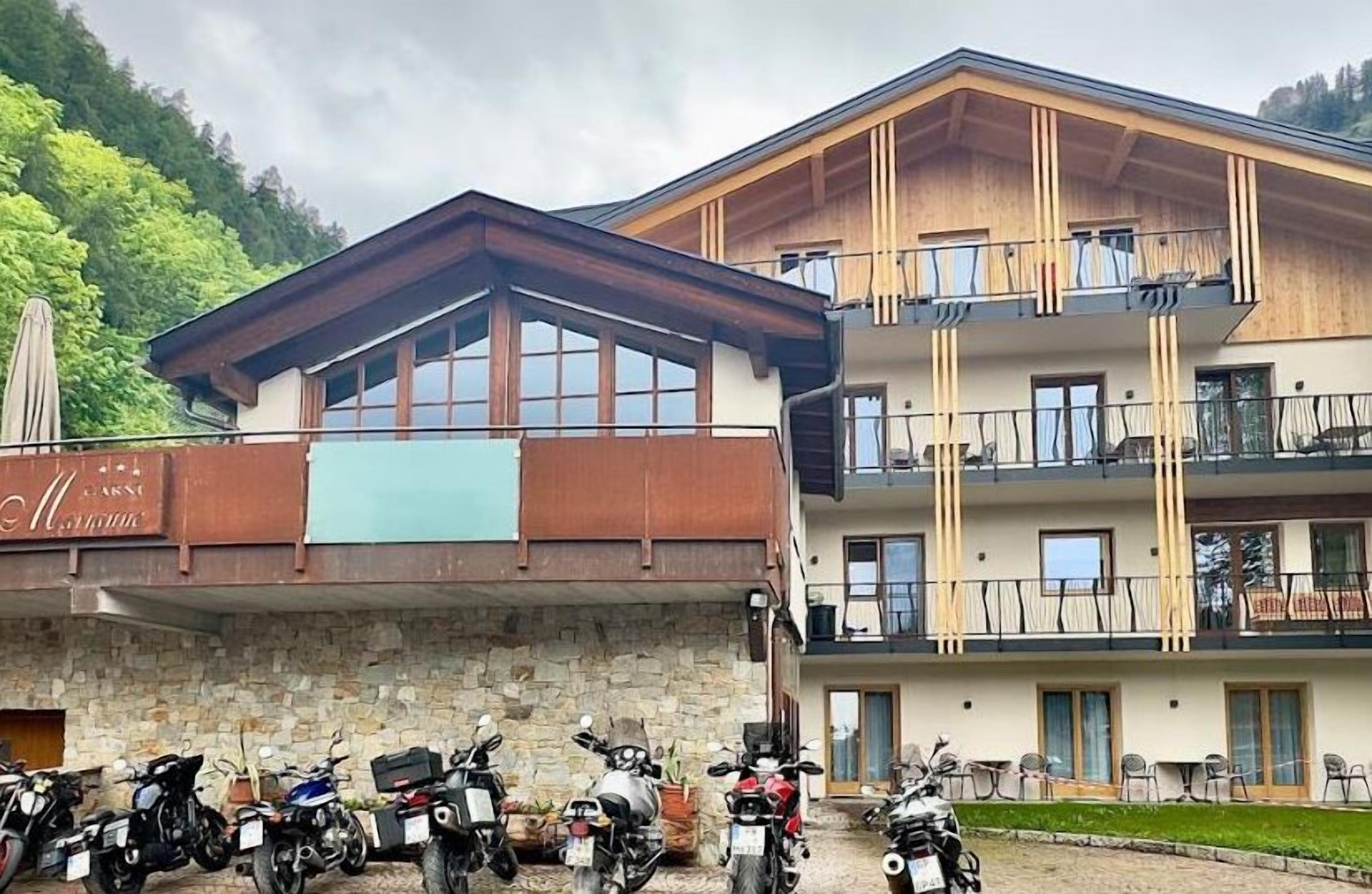 Un hôtel à la façade en pierre, avec un étage supérieur en bois doté de balcons, et une rangée de motos garées devant.