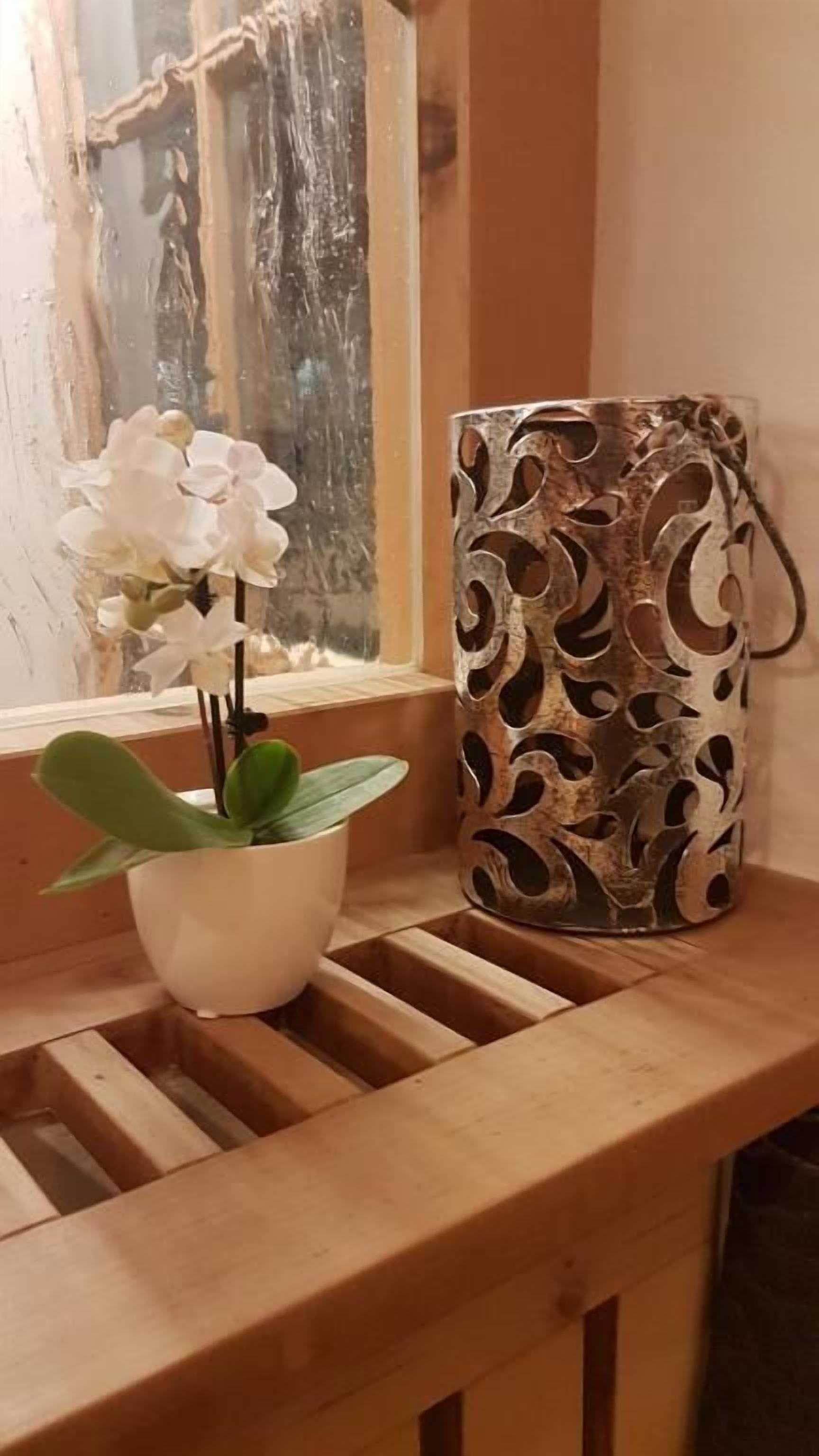 A wooden bench with a potted orchid and a decorative metal vase.