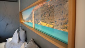 Una habitación con una cama, almohadas y un cuadro enmarco que representa un paisaje costero.