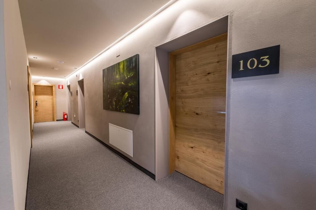 Un pasillo con una puerta de madera identificada con el número '103', un extintor y un cuadro en la pared.
