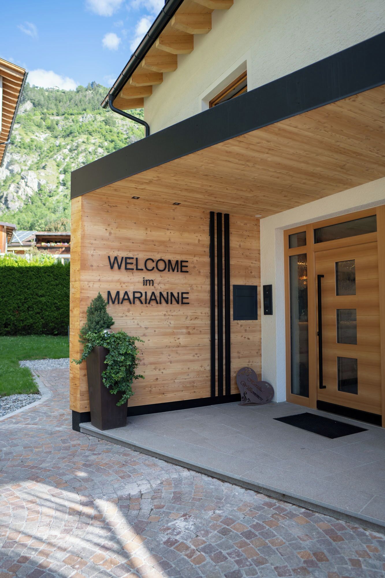 A modern building with a wooden facade and a welcoming sign that reads "WELCOME im MARIANNE".