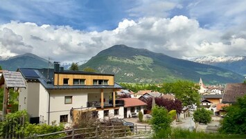 Un edificio moderno con techo plano y paneles solares, rodeado de casas tradicionales y un paisaje montañoso.