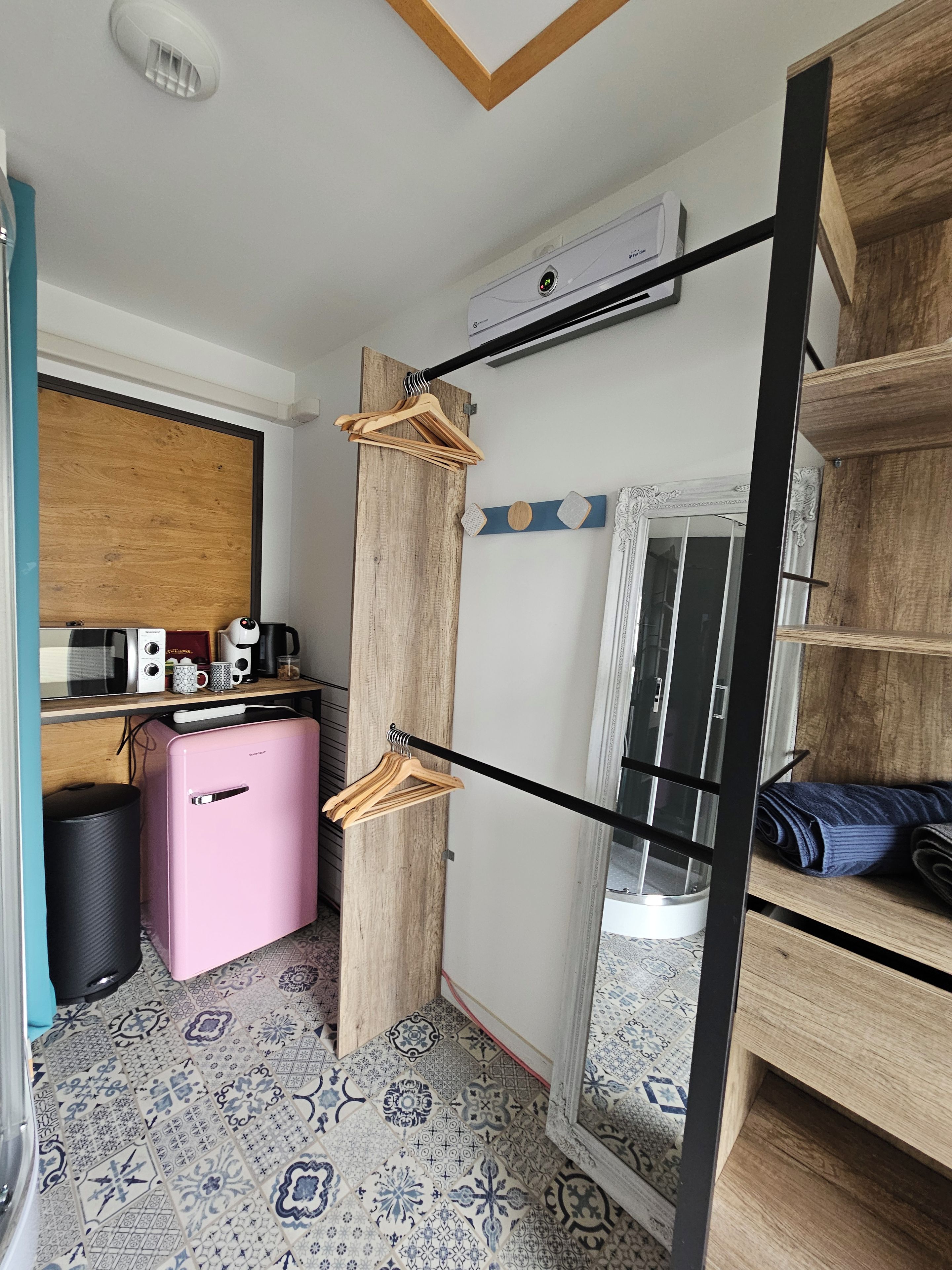 Une pièce compacte comprenant un coin cuisine, une armoire en bois, un miroir et un sol à motifs.