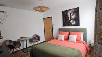 A bedroom with a bed, a desk, a chair, a hanging light fixture, and a door.