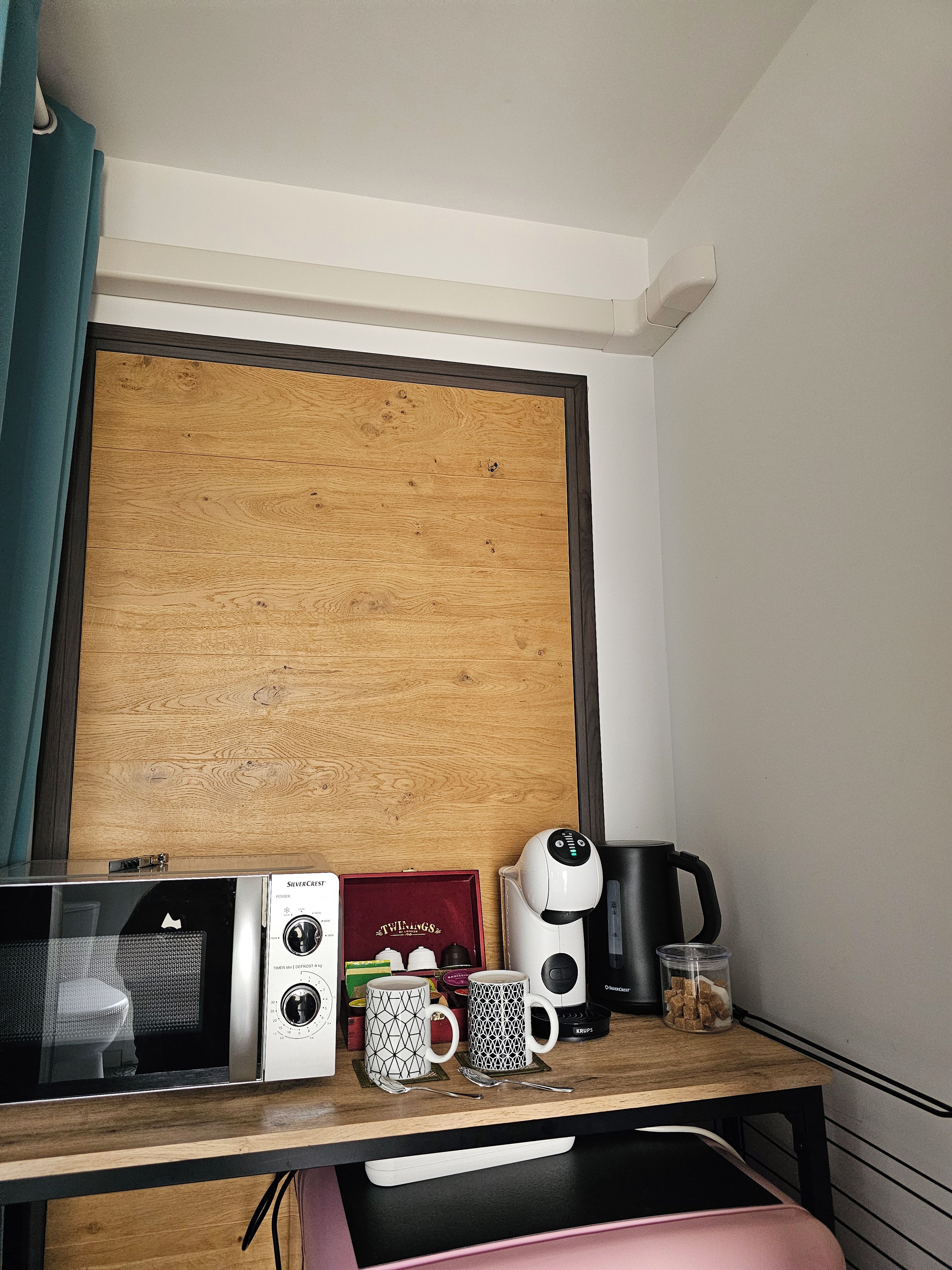 Une petite cuisine équipée d’un four à micro-ondes, d’une machine à café et d’une tasse, le tout posé sur un plan de travail en bois.