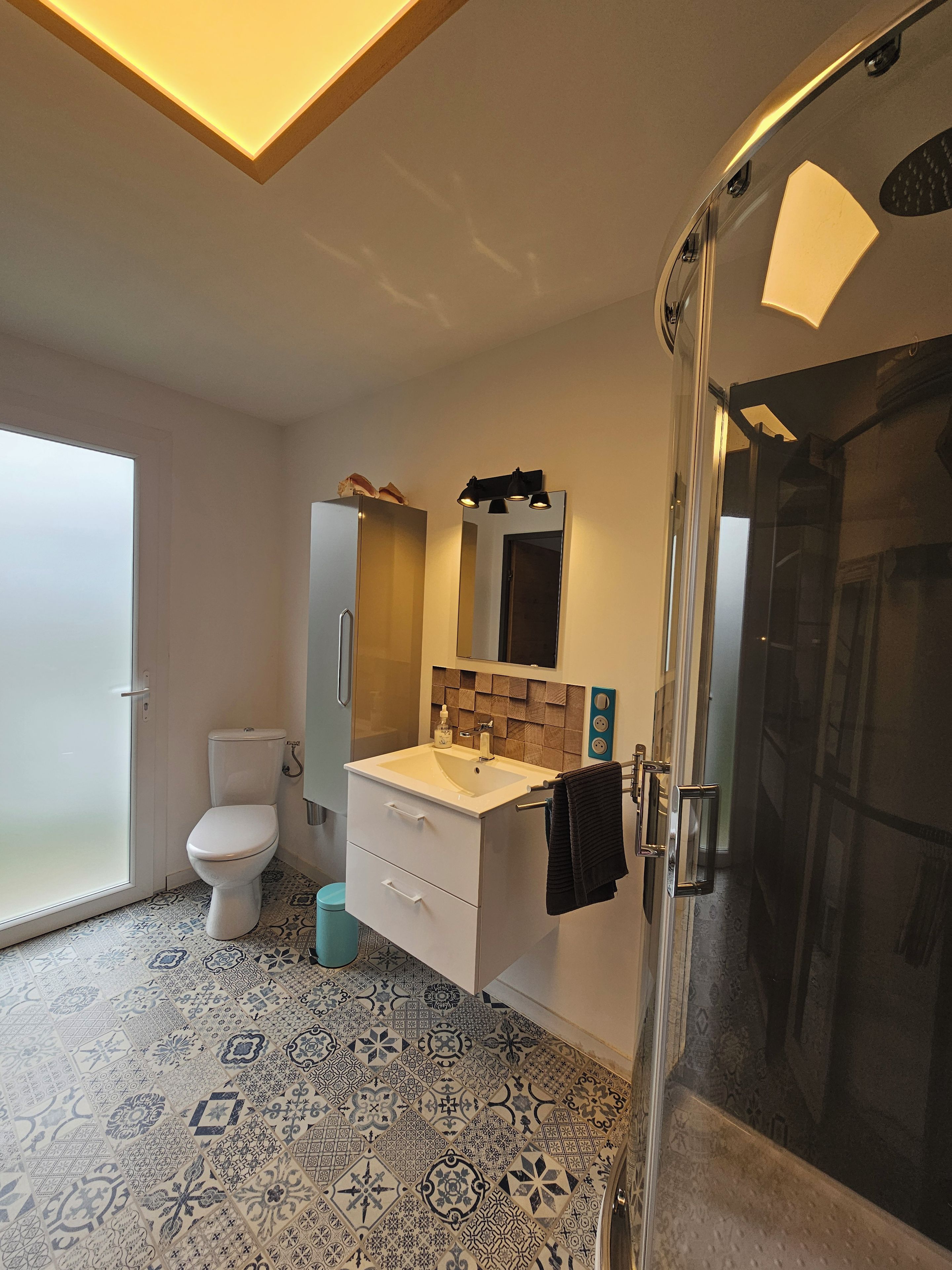 A modern bathroom with a glass shower enclosure, a white toilet, and a sink with a mirror above it.