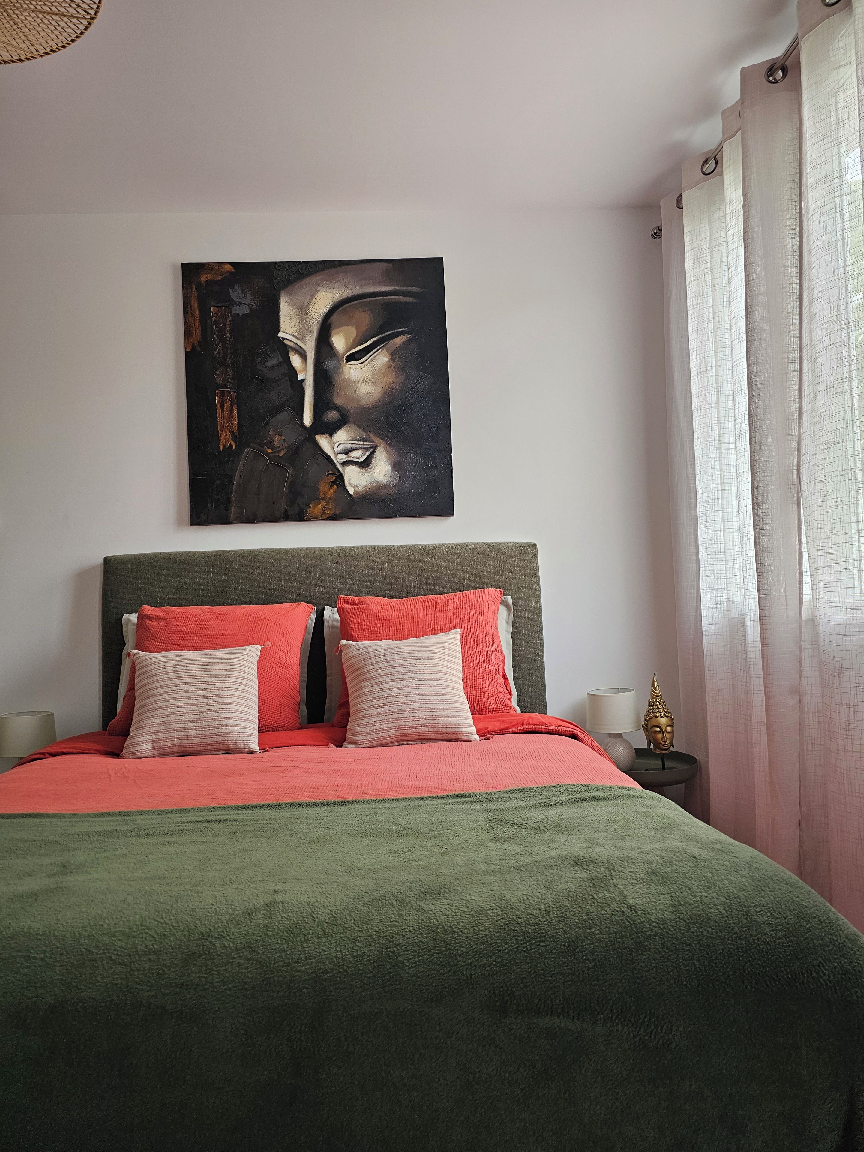 Un lit avec une literie rouge et verte, une tête de lit et un tableau accroché au mur.