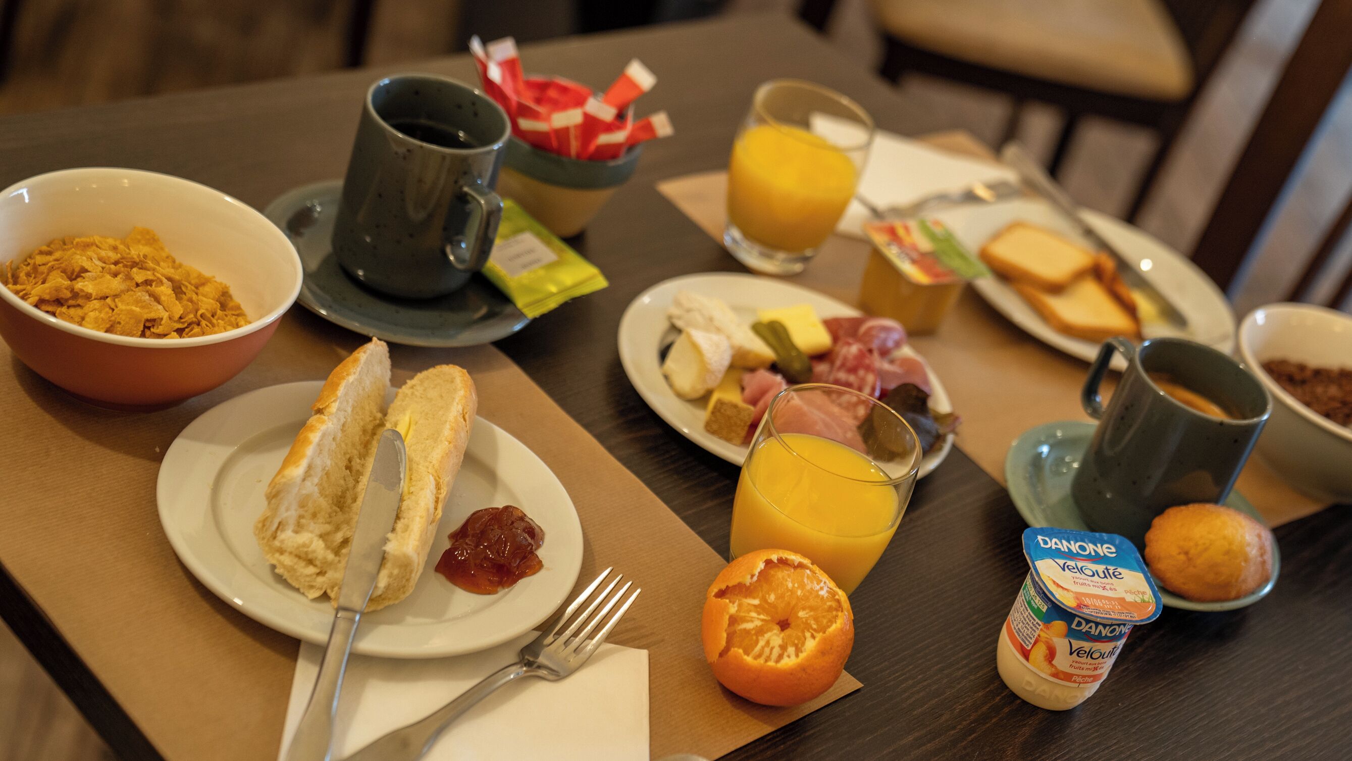 Una mesa de desayuno con diferentes alimentos y bebidas, como cereal, tostadas, fruta y jugo.