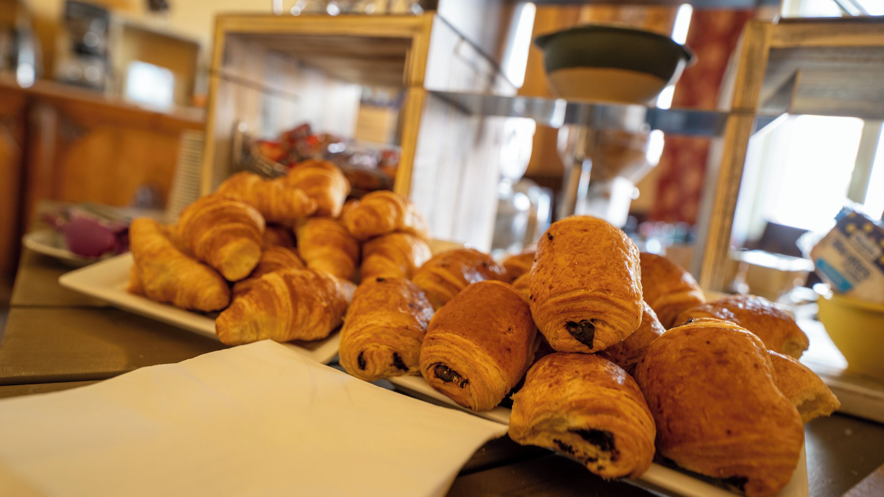 Une variété de pâtisseries est exposée, notamment des croissants et des viennoiseries fourrées au chocolat, dans une boulangerie.