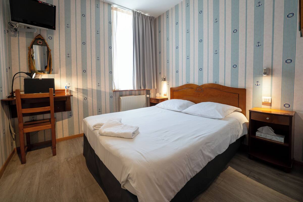 Une chambre d’hôtel équipée d’un lit, d’un bureau, d’une chaise, d’une télévision et d’une fenêtre avec des rideaux.