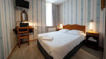 A hotel room with a bed, a desk, a chair, a television, and a window with curtains.