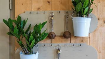 A wall-mounted wooden rack with two white buckets holding green plants, a metal hook, and a whiteboard.