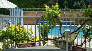 Een zwembadterras met een overdekte patio, rieten meubels en uitzicht op een zwembad en groen.