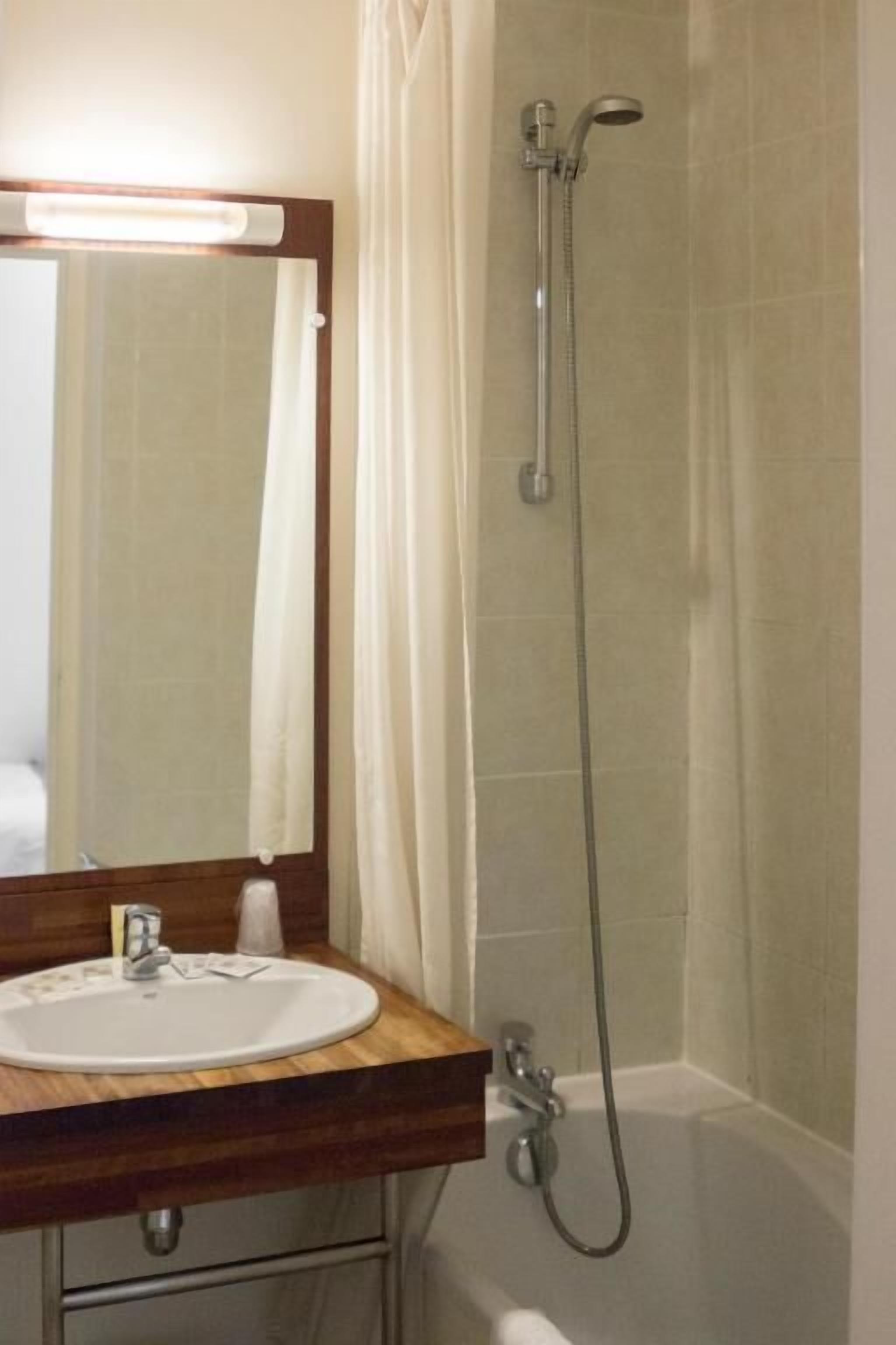 Een badkamer met een houten wastafel, een witte wasbak, een spiegel, een douche en een bad.