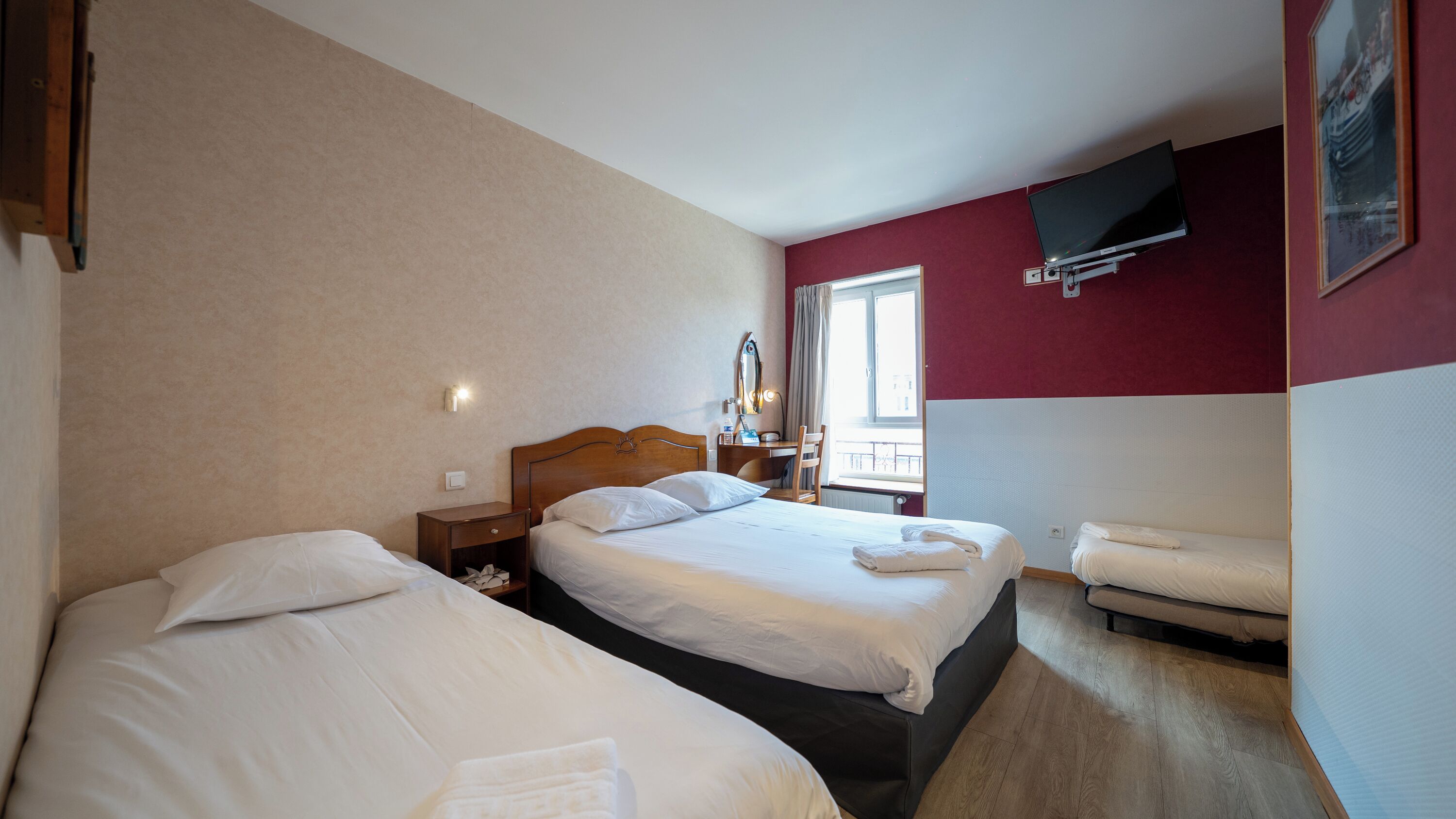 Habitación de hotel con dos camas, un escritorio, una silla, un televisor y una ventana.