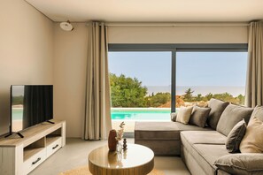 Una sala de estar moderna con un gran ventanal, un televisor de pantalla plana, un sofá y una mesa de centro.