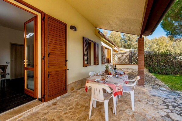 A patio with a stone floor, a table set with plates and glasses, and a wooden door.