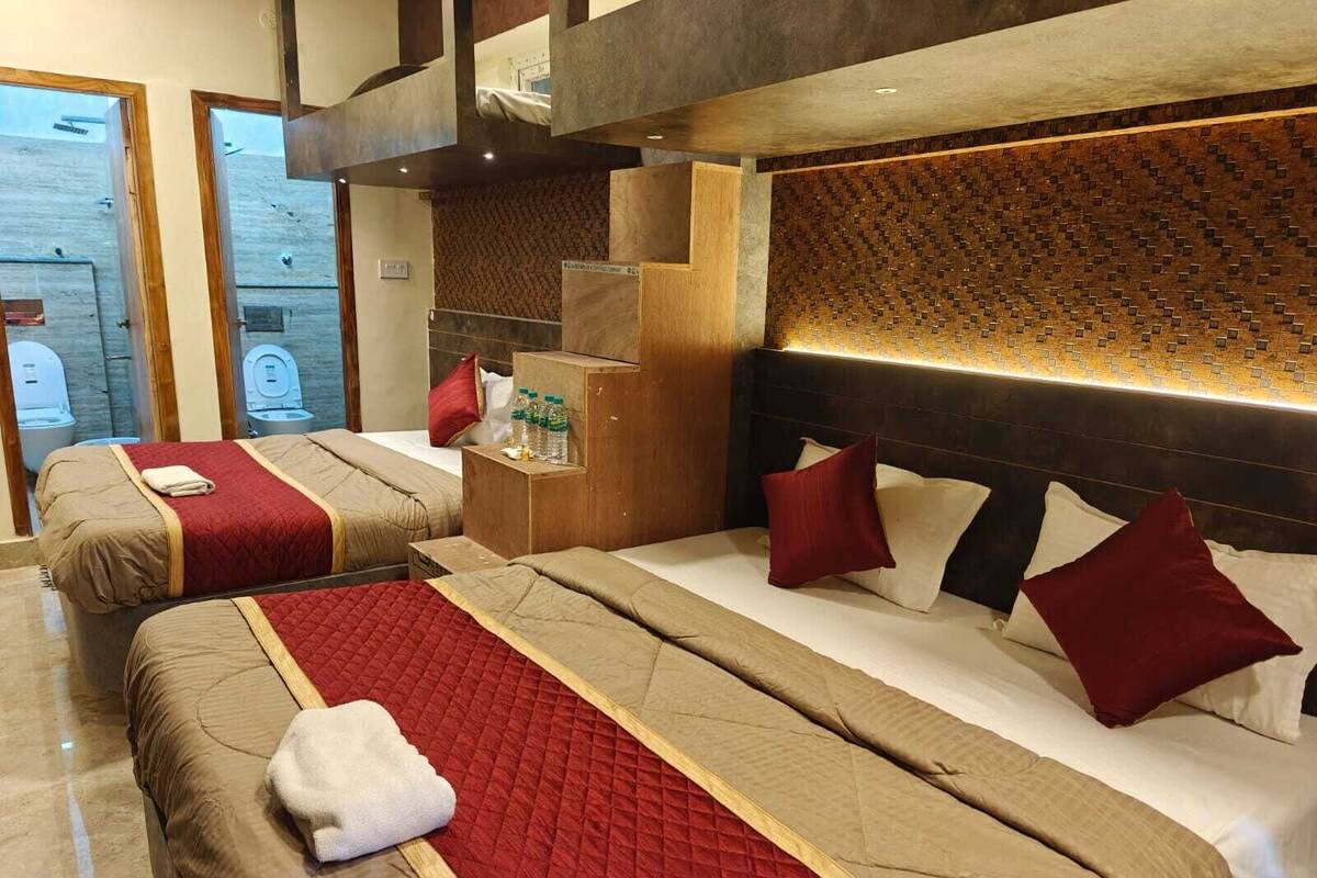 Habitación de hotel con dos camas, cabecera de madera, un pequeño armario de madera y vistas al exterior.