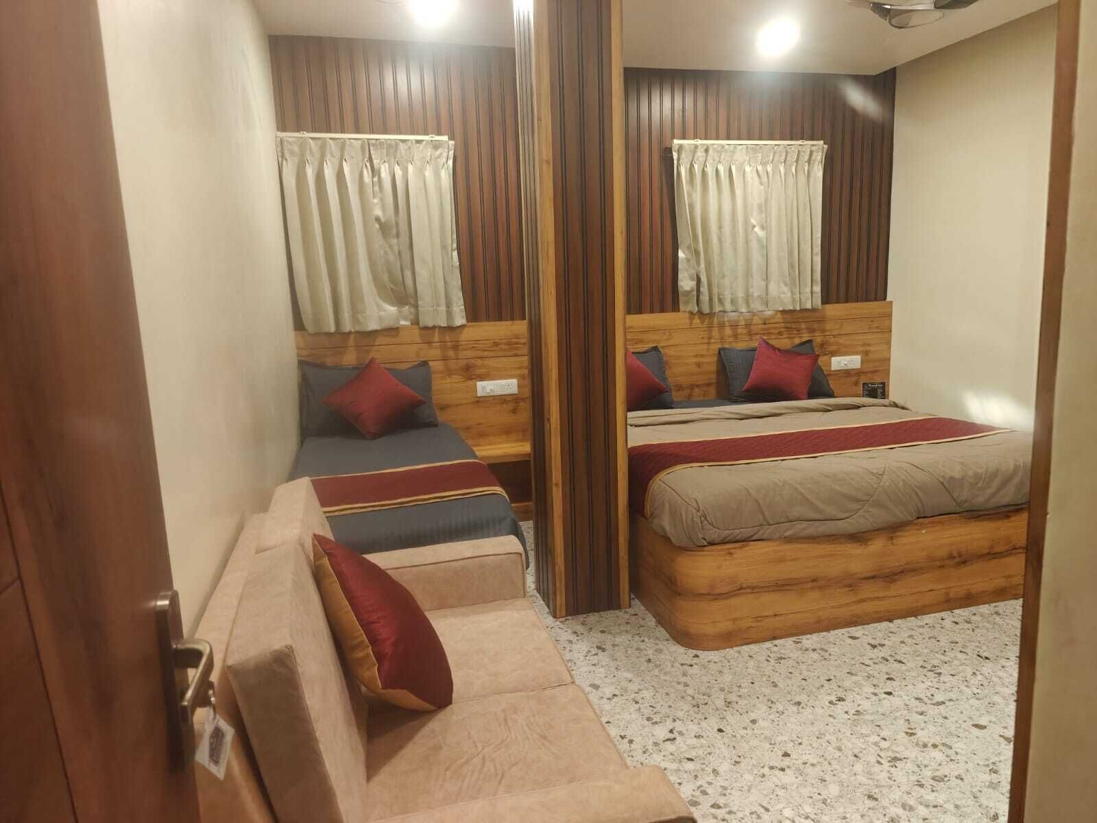 Quarto com duas camas, cabeceiras de madeira, um pequeno sofá e piso coberto por carpete.