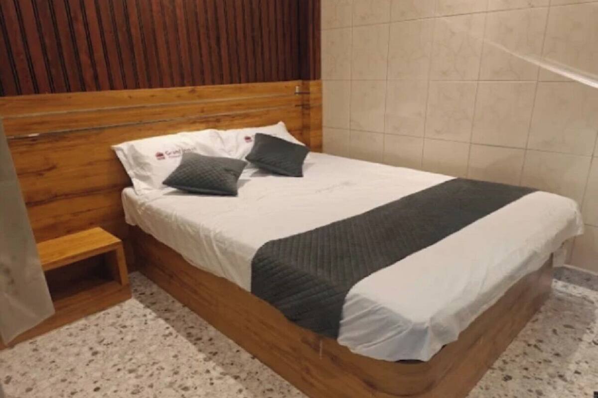 Una cama de madera con una manta blanca y gris, una mesita de noche de madera y un cabecero de madera.