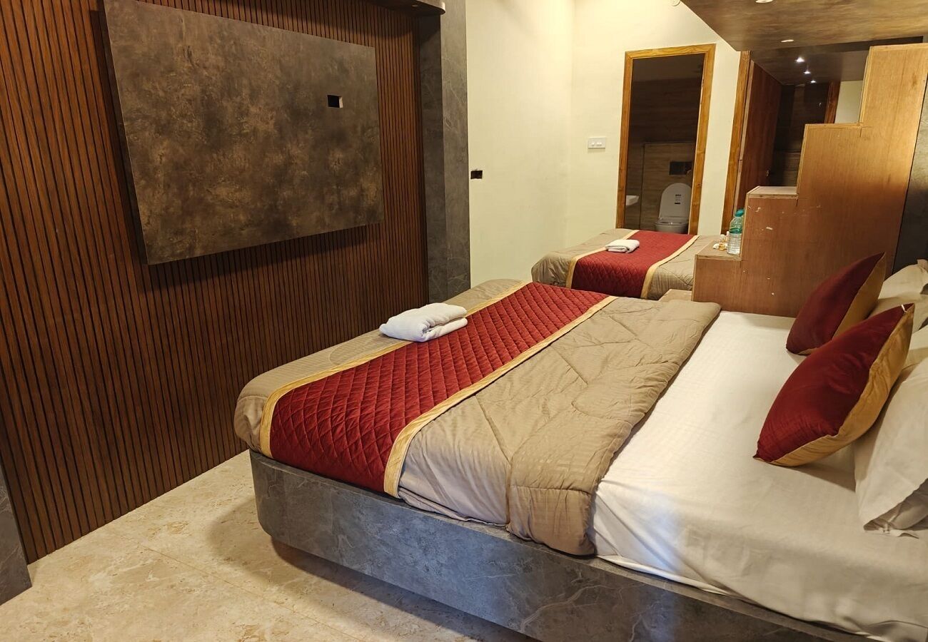 Habitación de hotel con una cama grande, un panel de pared de madera, un televisor montado y un baño visible a través de una puerta abierta.