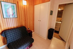 Et værelse med en ternet sofa, et garderobeskab, et lille bord med en lampe og en skraldespand.
