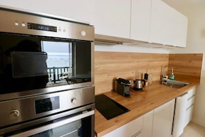 A modern kitchen with stainless steel appliances, a wooden countertop, and a view through the window.