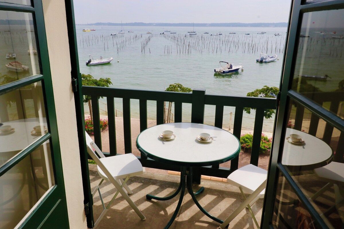 Un balcone con tavolo e sedie, vista su un corpo d'acqua con barche e pali di legno.