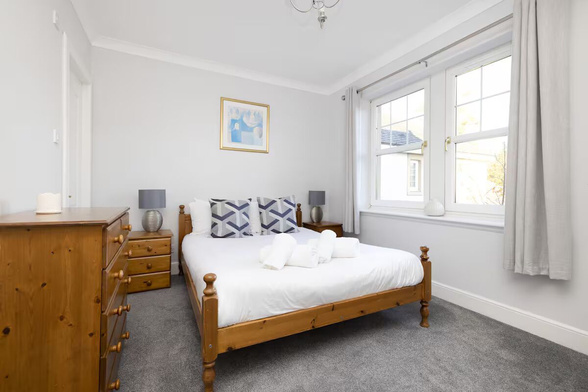 A neatly arranged bedroom with a wooden bed, a dresser, and a window with curtains.