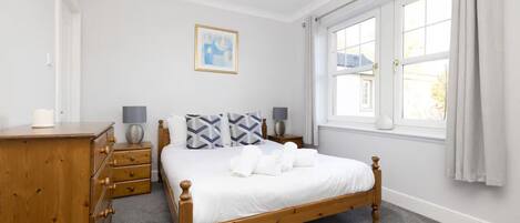 A neatly arranged bedroom with a wooden bed, a dresser, and a window with curtains.