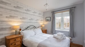 Una cama bien tendida con ropa blanca, una lámpara de noche y una mesita de noche de madera con cajones.