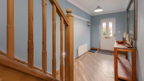 Una escalera de madera que conduce a una habitación con una puerta blanca, un radiador y una pequeña mesa con un cuenco y un adorno.
