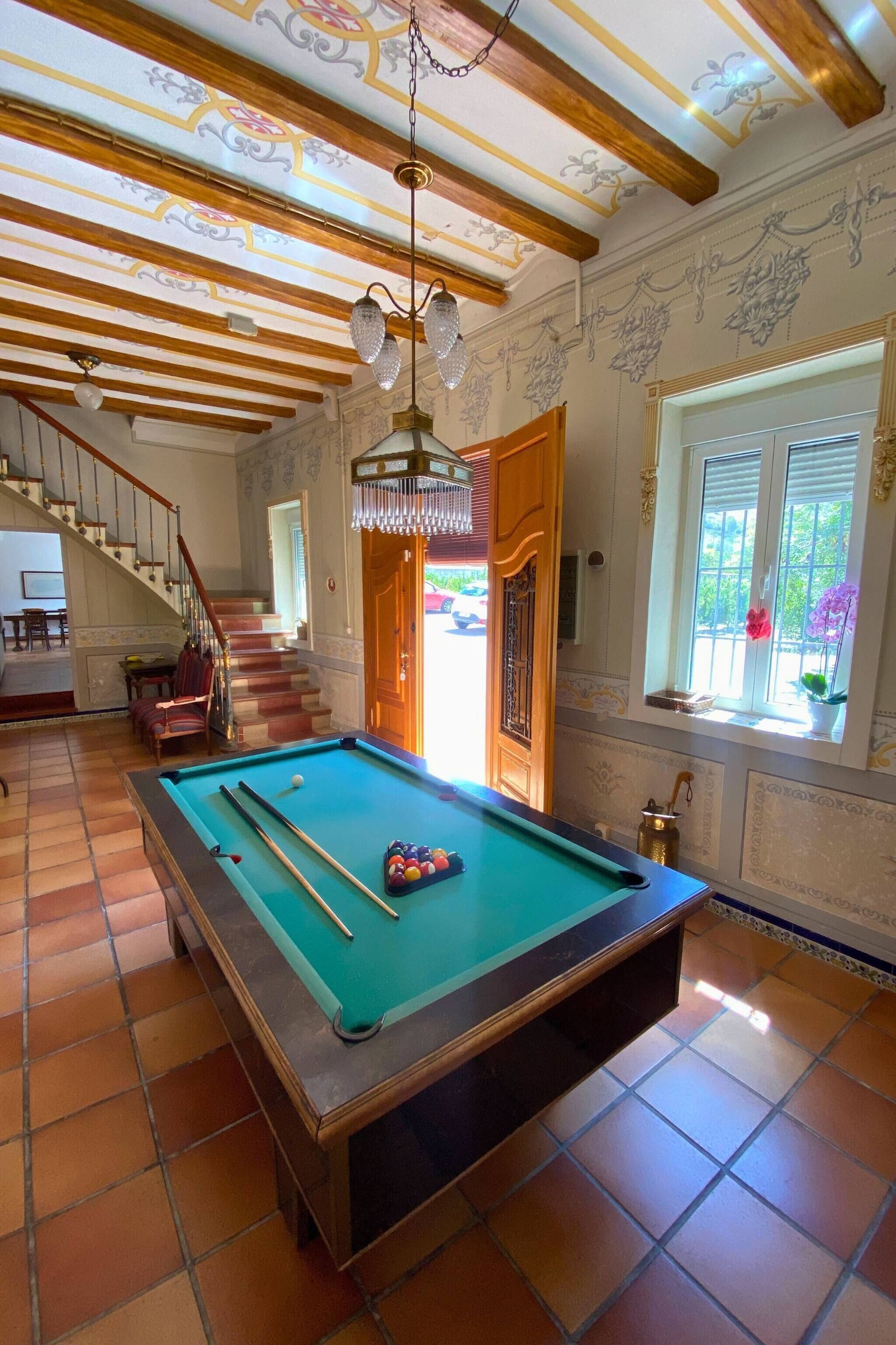 Una mesa de billar en una habitación con una escalera, vigas de madera y un candelabro.