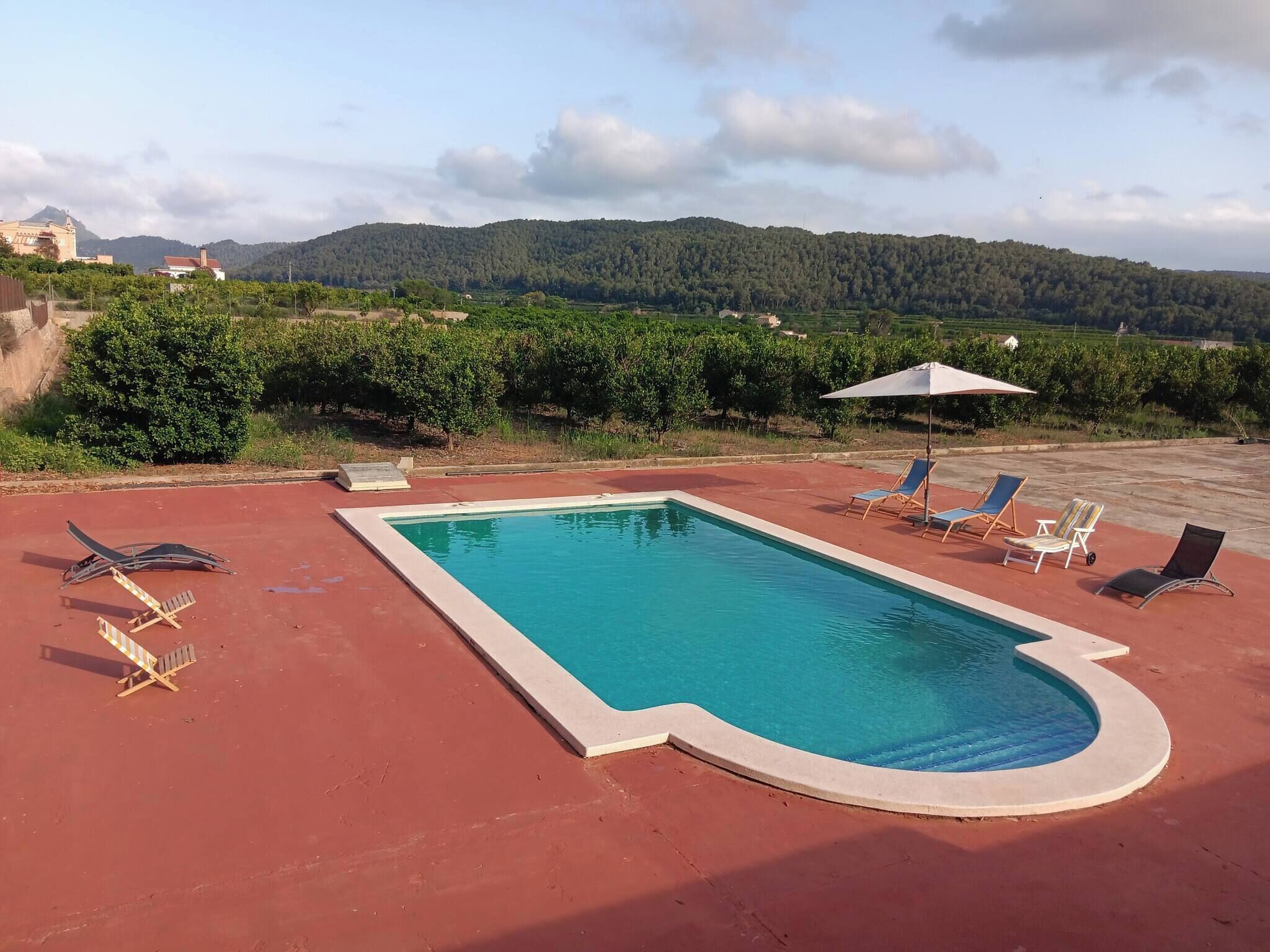 Ein rechteckiger Pool mit roter Liegefläche, umgeben von Liegestühlen und Sonnenschirmen.