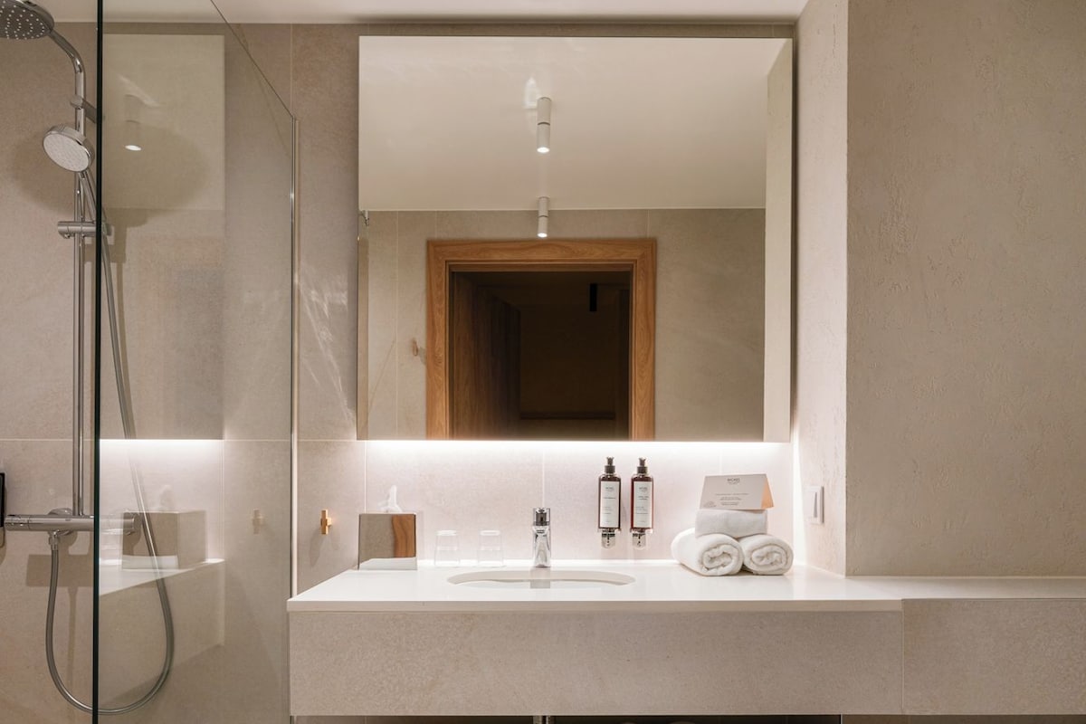 A modern bathroom with a glass shower enclosure, a large mirror, and a built-in sink with a wooden shelf below.
