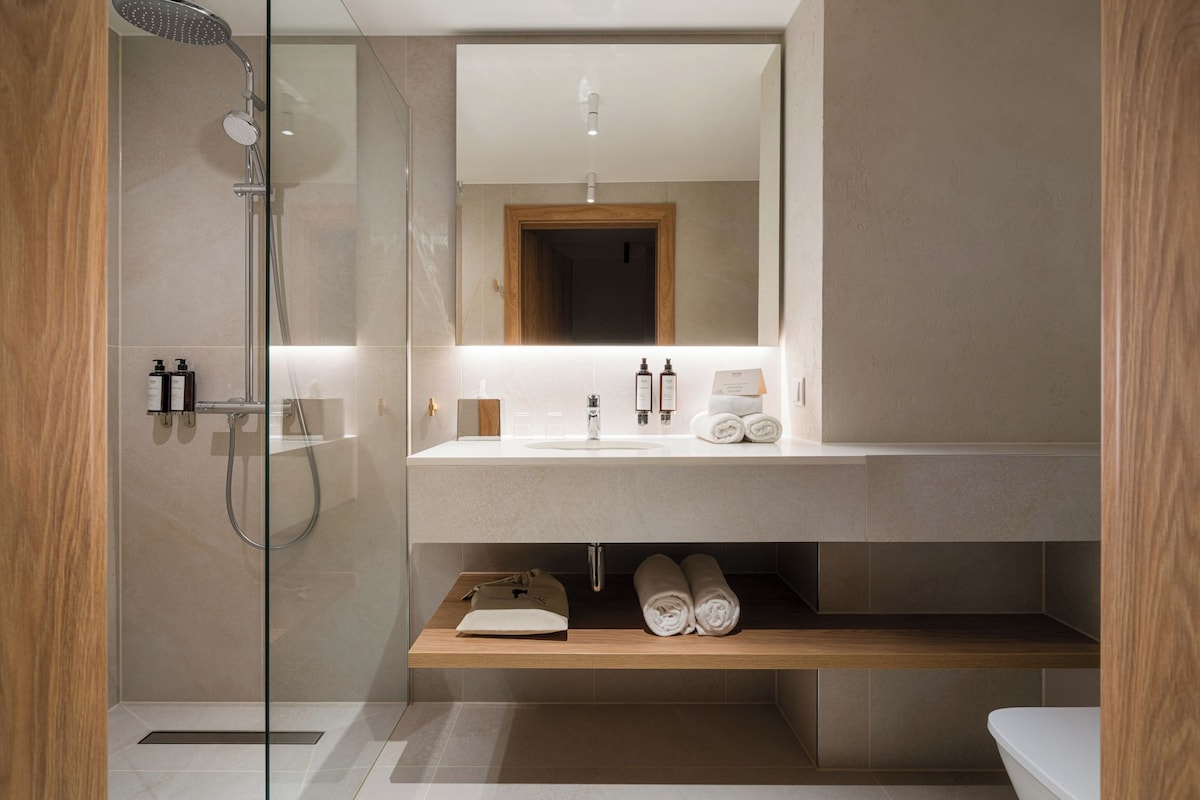 A modern bathroom with a glass shower enclosure, a wooden vanity, a mirror, and a towel rack.