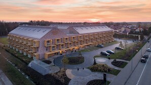 A modern building with a unique geometric facade and multiple balconies, surrounded by a landscaped area with a central circular driveway. - Nickel Resort & Wellnest Grzybowo (Grzybowo)