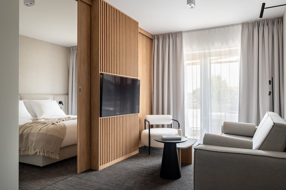 Quarto de hotel moderno com cama, televisão, sofá, poltrona e pequena mesa.