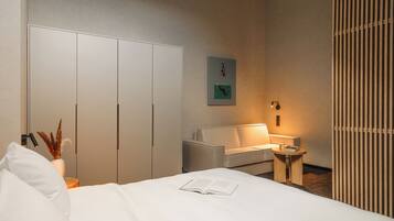 A hotel room with a bed, a sofa, a small table, a lamp, and a wardrobe.