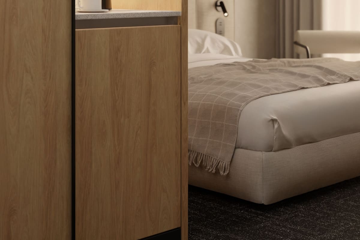 Quarto de hotel moderno com uma kitchenette em madeira, uma cama com manta bege e vista para a cidade pela janela.