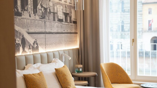 A hotel room with a large bed, a chair, a table with a coffee maker, and a view of the city through the window. - Anna Teresa Luxury (Pisa)