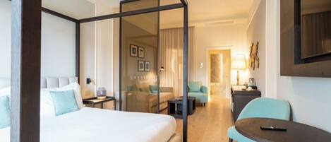 Ein Hotelzimmer mit einem großen Bett, einer Sitzecke mit einer Couch und Sesseln, einem kleinen Tisch und einem an der Wand befestigten Fernseher.