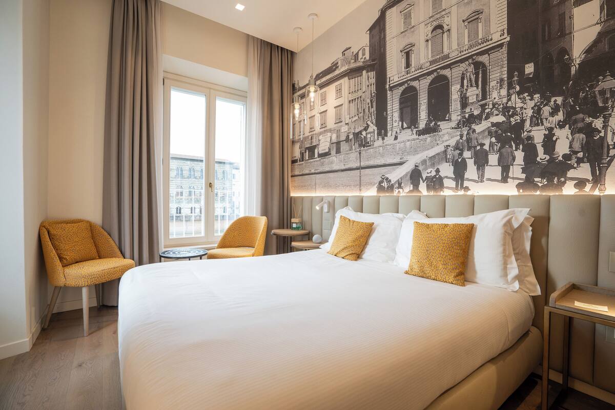 A hotel room with a large bed, two armchairs, a small table, and a large wall mural.