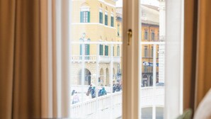 A hotel room with a view of a clock tower and buildings through a window with curtains. - Anna Teresa Luxury (Pisa)