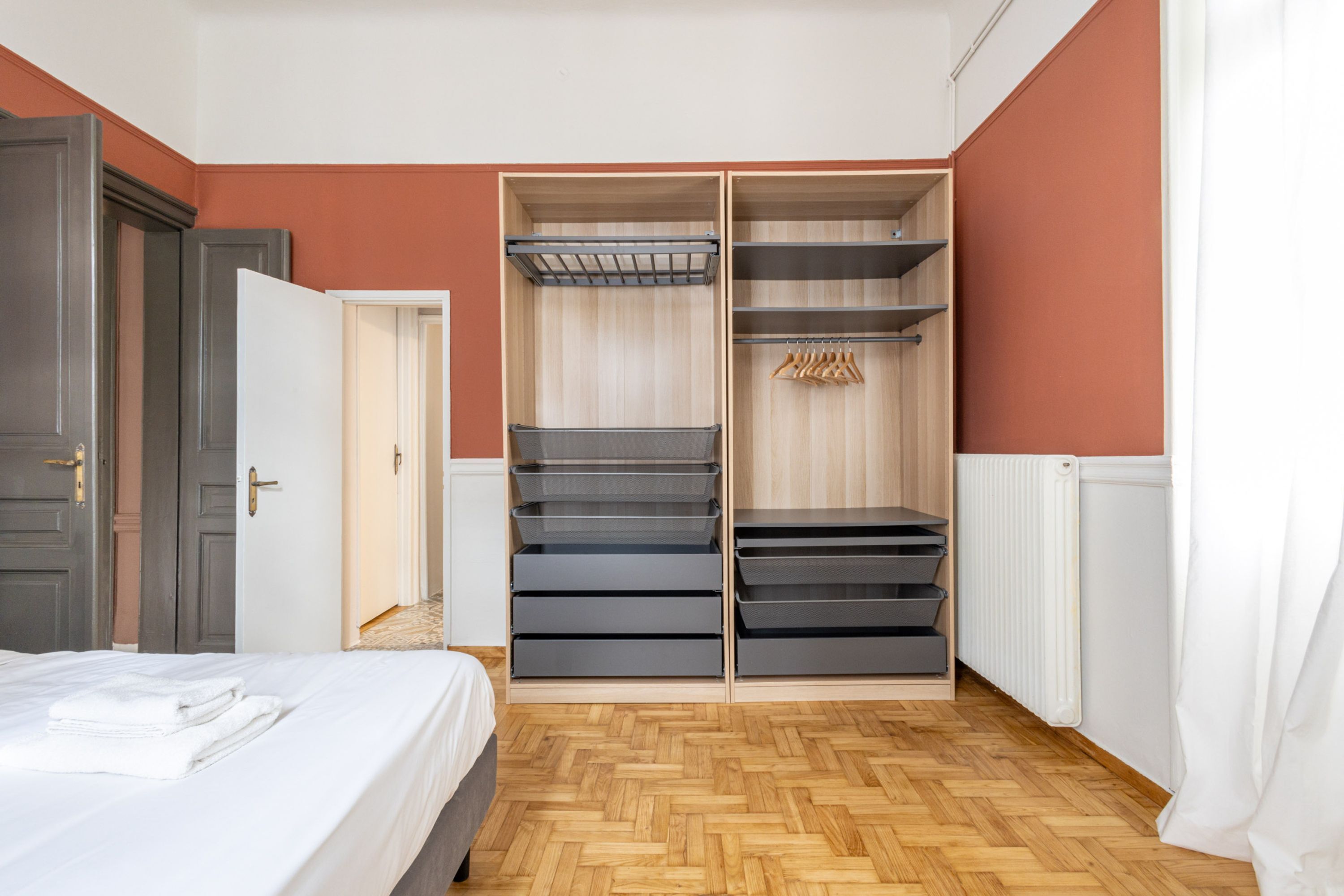 A bedroom with a bed, a wardrobe with multiple drawers and shelves, and a radiator.
