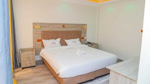 Una cama bien hecha con ropa de cama y almohadas blancas, un cabecero de madera, una mesita de noche y una pequeña mesita auxiliar de madera.