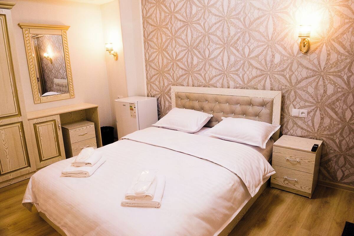 A neatly made bed with a headboard, two bedside tables, a mirror, and a wall-mounted light fixture.